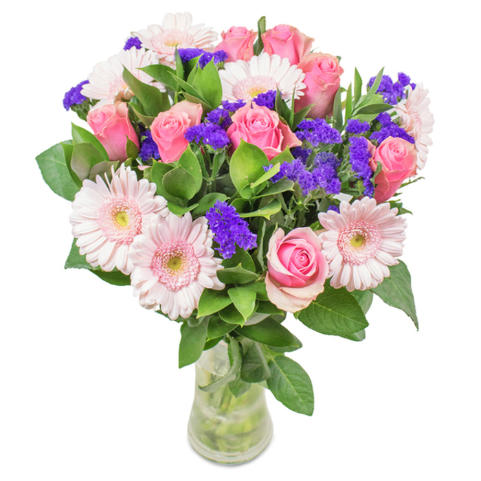 Against a pristine white background, this artfully designed bouquet from Walworth Florist showcases a harmonious arrangement of approximately eight pink roses, their petals at various stages of unfurling, creating a captivating spiral pattern. The roses are complemented by five to seven pale pink Gerbera daisies with radiant centres, their broad petals forming soft halos of gentle colour. Carefully spaced among the main blooms are clusters of vivid purple statice, their textured forms adding lively contrast and echoing the vibrancy of Walworth's bustling street corners. Lush, deep green foliage winds gracefully throughout, providing a fresh, abundant visual anchor reminiscent of the greenery found in local community gardens. The clear glass vase serves as a crystal frame, enhancing the natural light and drawing attention to the intertwining stems and water below-signs of freshness and local pride. Ideal for a wide range of occasions, from birthdays and anniversaries to thoughtful everyday gestures, this bouquet encapsulates the warmth, celebration, and diversity of Walworth itself, inviting a sense of local joy and heartfelt affection into any space.